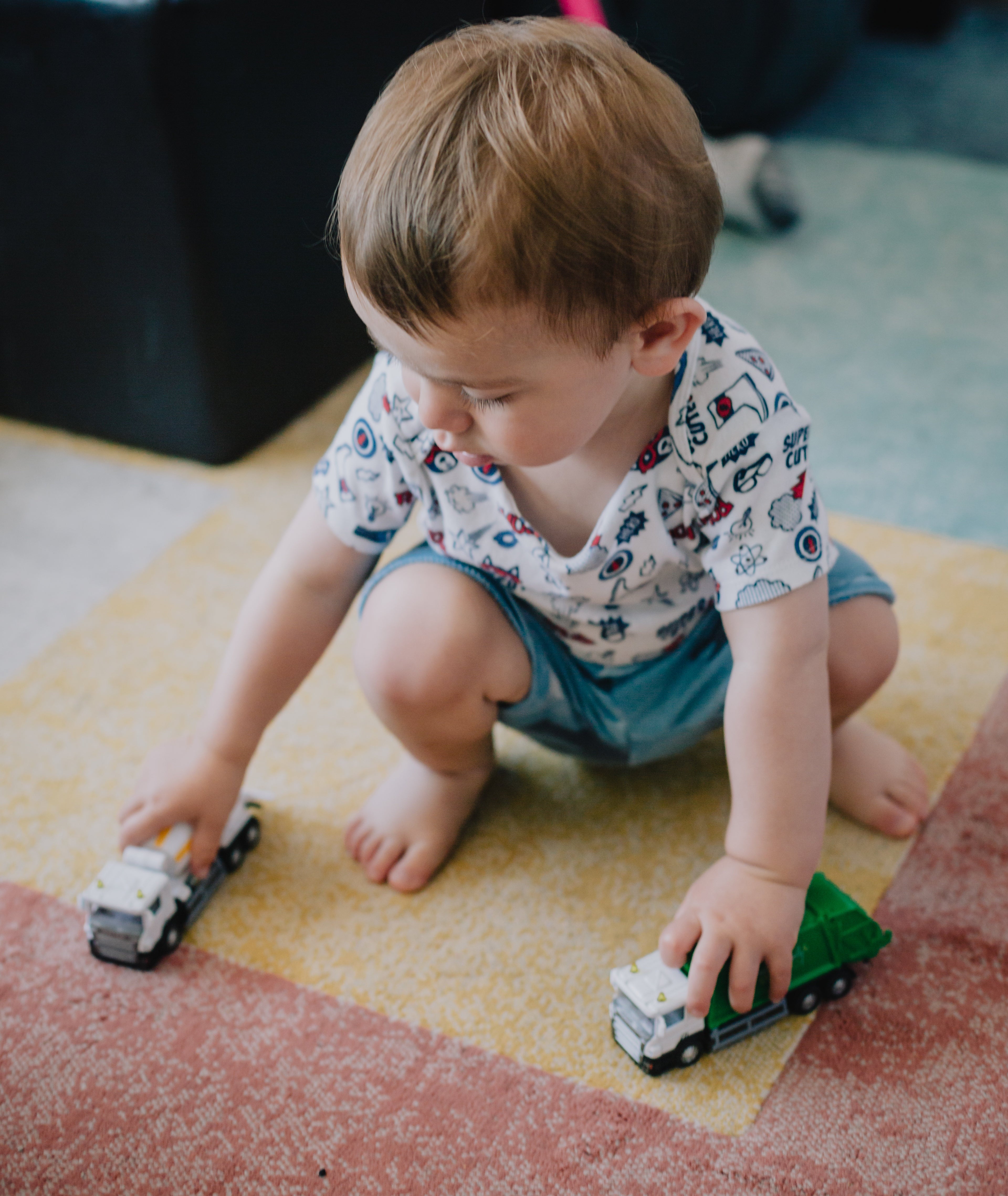 Toddler playing with toy trucks on colorful rug in collection of Boys Stylish Apparel & Toys for Every Personality 