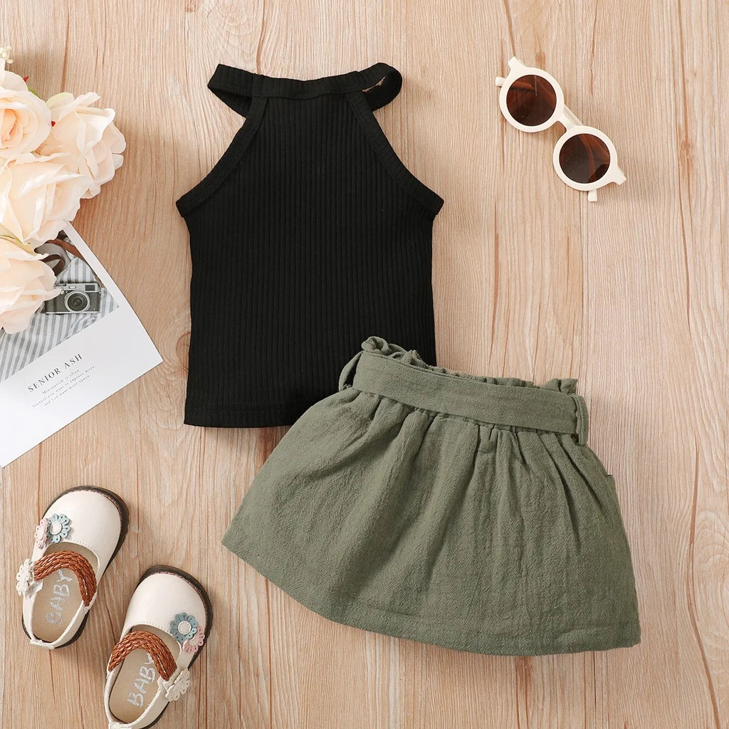2PCS Baby Girl Clothing Set with black sleeveless top and olive green skirt on wooden background