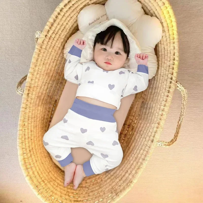 Baby wearing Baby 2PCS Pajama Set Cotton Long Sleeve Outfit for Autumn Winter Wear with heart patterns lying in a woven basket