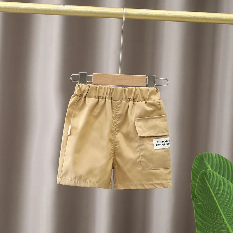 Beige shorts from baby boy clothes set by Yamza Tots' Closet hanging on wooden hanger