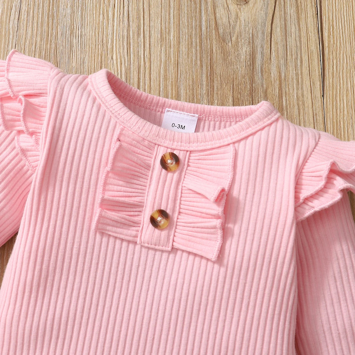 Yamza Tots' Closet pink ribbed baby girl bodysuit with ruffle details and buttons on wooden background