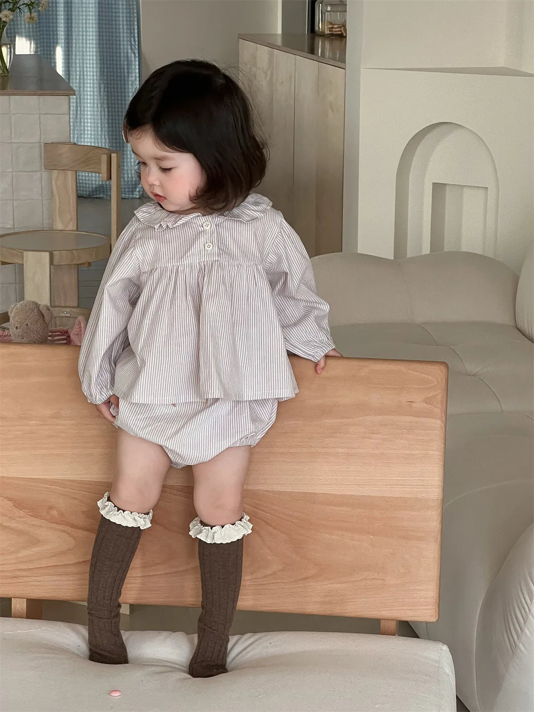 Baby girl wearing a Baby Girl Loose Striped Set with long sleeves and matching shorts in a cozy living room