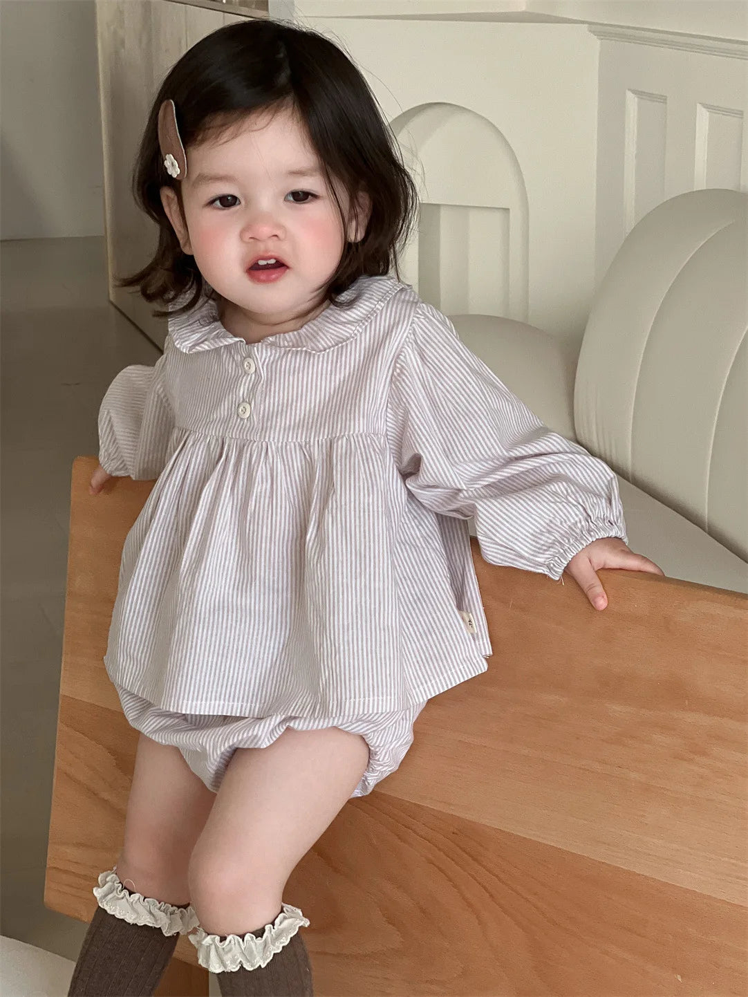 Baby girl wearing a loose striped Baby Girl Loose Striped Set sitting on a wooden bench indoors