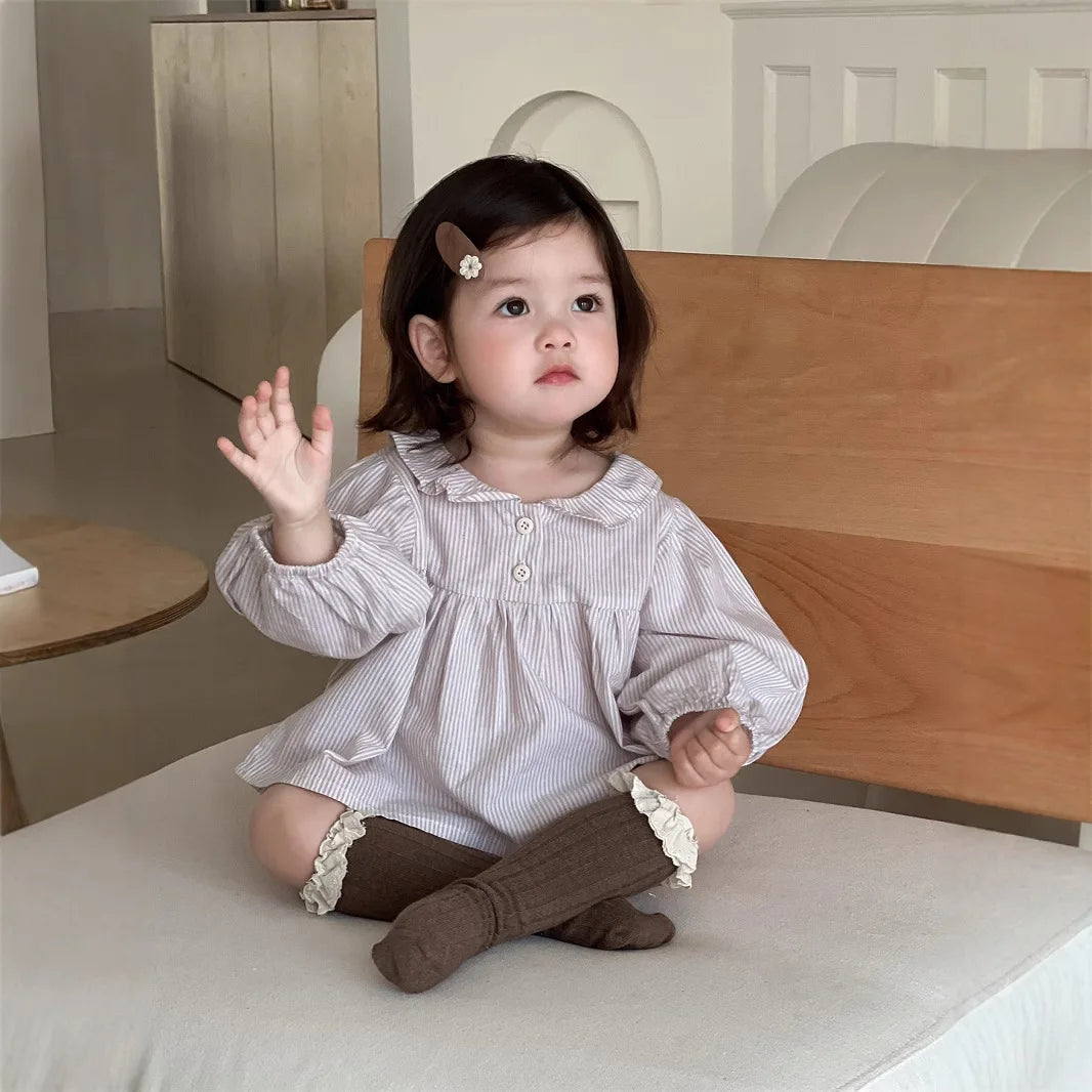 Baby girl wearing a Baby Girl Loose Striped Set sitting on a couch with brown socks and hair clip