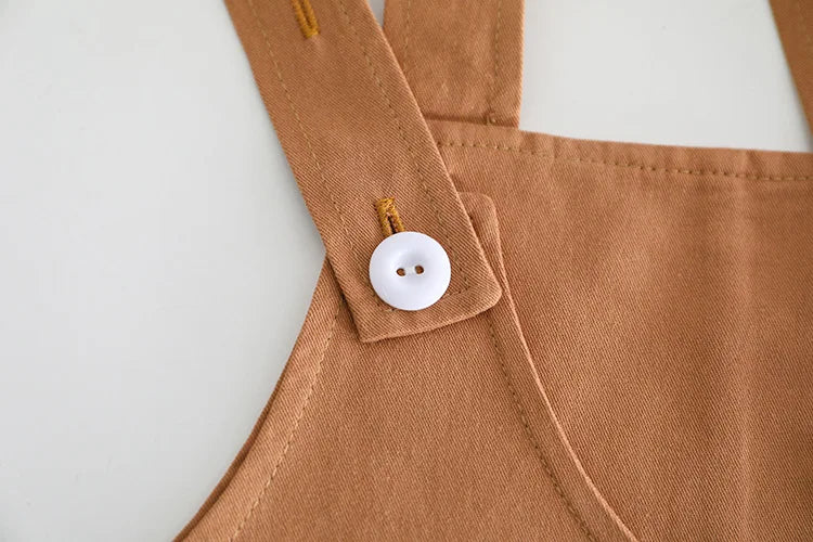 Close-up of brown fabric strap with white button detail on baby girls and boys clothing