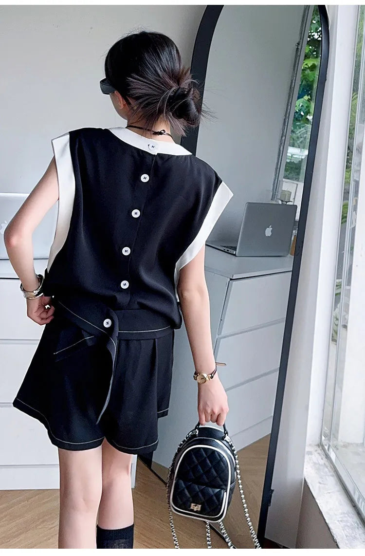 Back view of Black and White Spliced Vest and Shorts Two-Piece Casual Sports Outfit Set worn by woman holding black quilted handbag