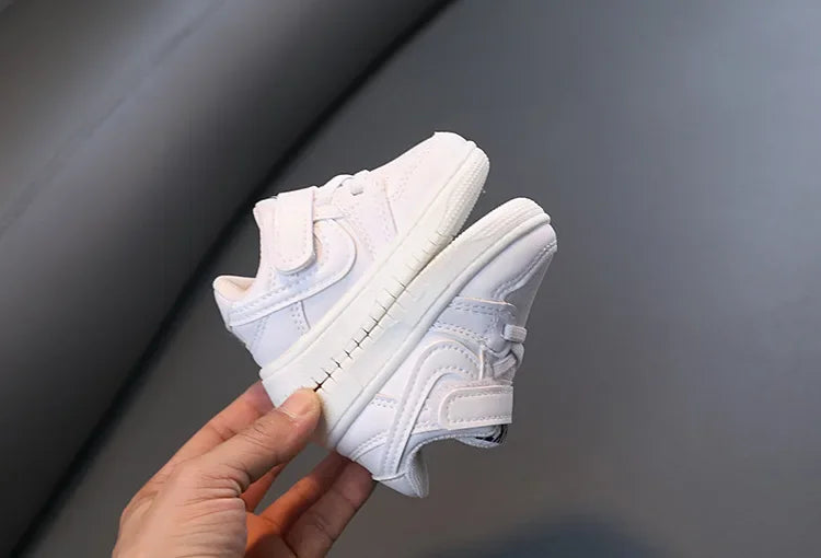 Children White Casual Sneakers Soft-Soled Running Shoes for Boys and Girls held in hand with velcro straps 