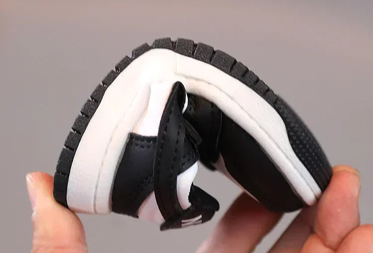 Flexible black and white children's sneakers by Yamza Tots' Closet being bent to show softness