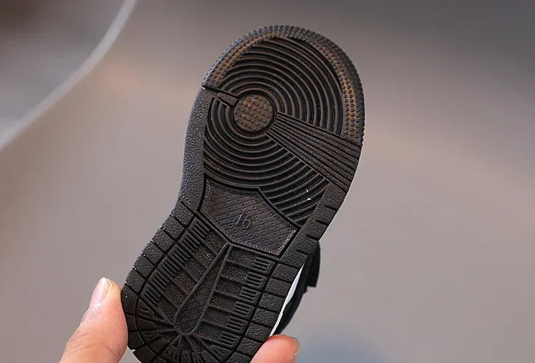 Black sole of a children's sneakers held by hand showing detailed tread pattern