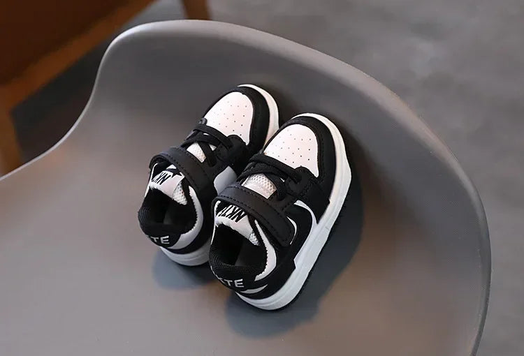 Black and white children's sneakers with velcro straps on a gray chair by Yamza Tots Closet