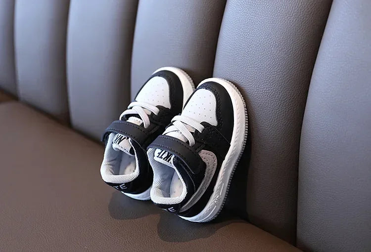 Black and white children's sneakers with laces and Velcro straps on brown leather couch