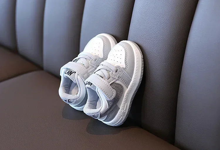 Yamza Tots' Closet white and gray children's sneakers with Velcro straps on brown leather couch