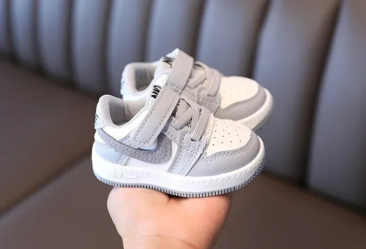 Yamza Tots' Closet white and gray Children's Sneakers with velcro strap held in hand