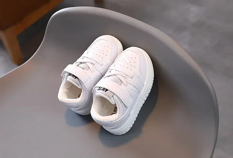 White Children's Sneakers with Velcro straps and perforated design on gray chair