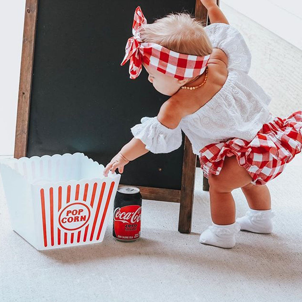 Cute Baby Girl Summer Set Off-Shoulder Lace Tops Red Plaid Dress and Headband worn by toddler near popcorn box