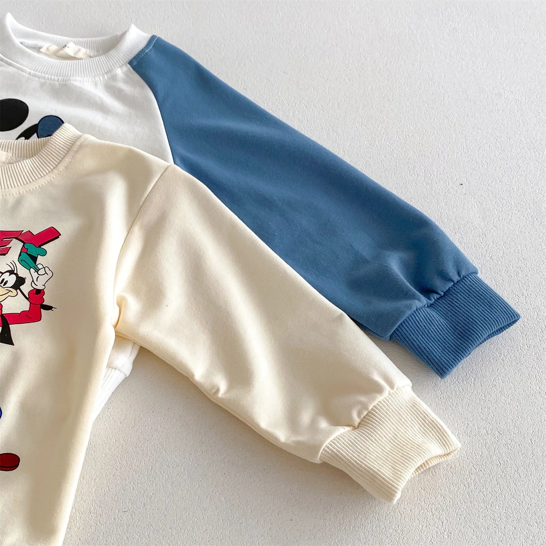 Close-up of Yamza Tots' Closet Disney Cartoon Tracksuit featuring cream and blue sleeves with cartoon character print
