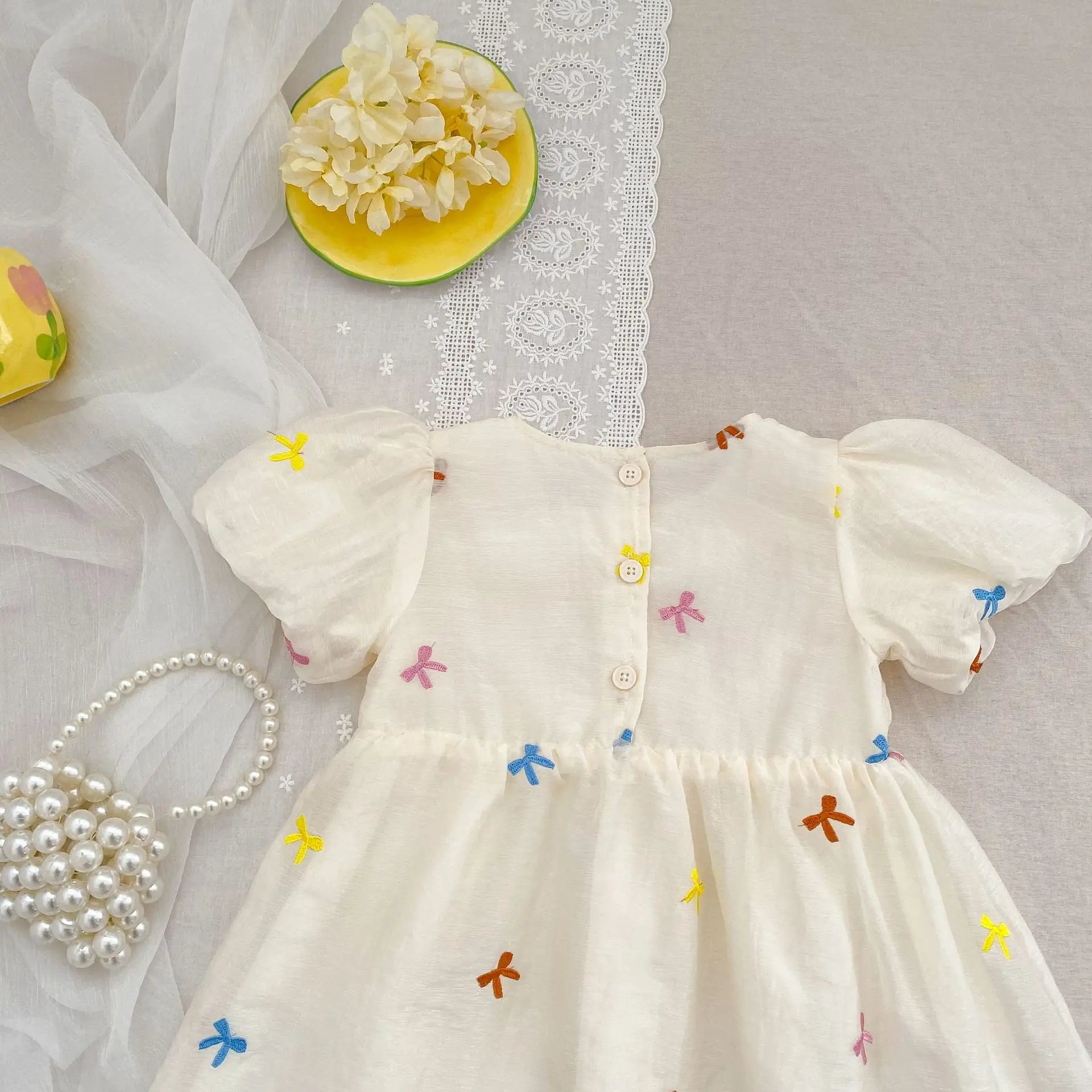 Fashion Baby Girls Embroidered Bow Puff Sleeve Cotton Backless Princess Dress laid flat with pearl bag and decorative flowers