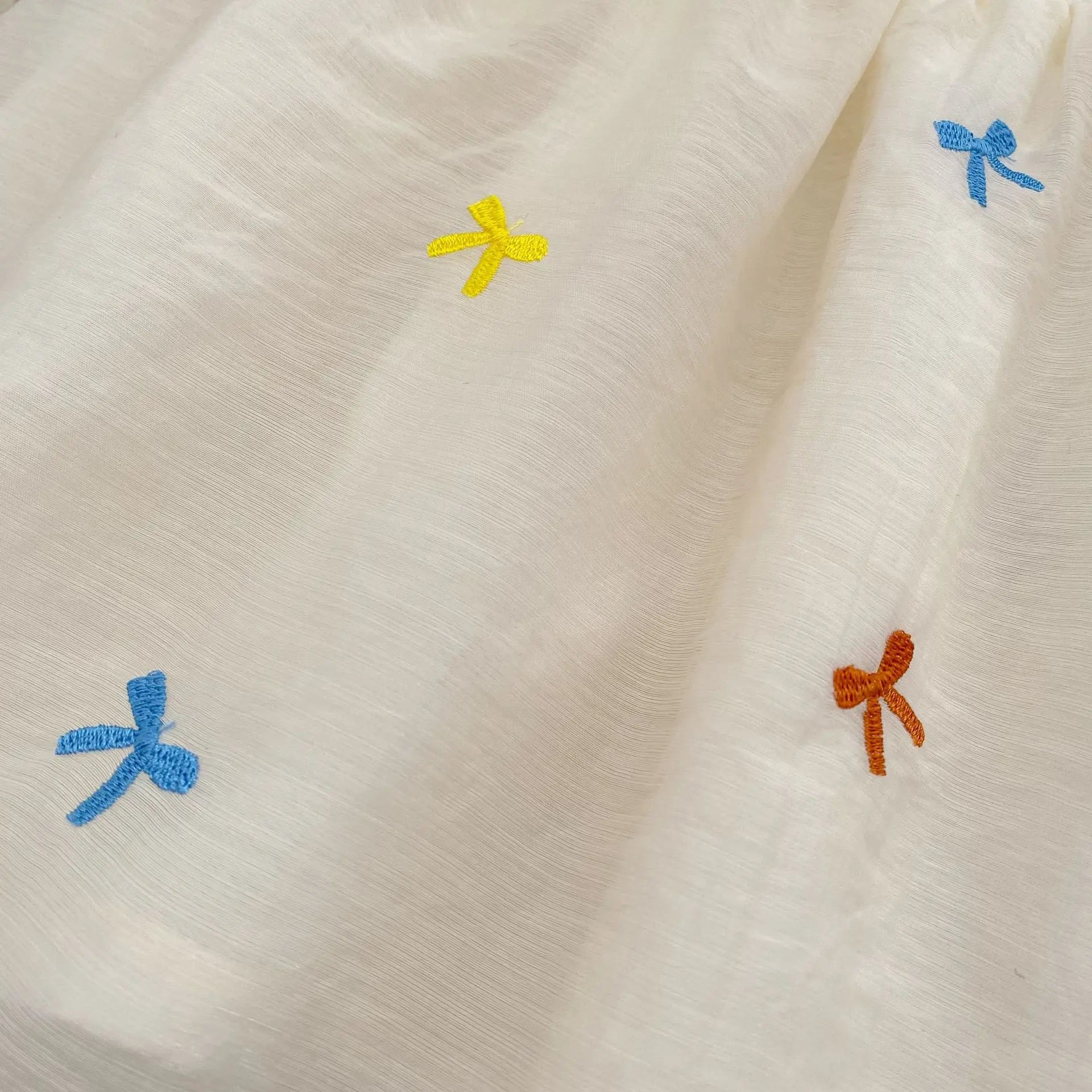Close-up of Fashion Baby Girls Embroidered Bow Puff Sleeve Cotton Backless Princess Dress with colorful embroidered bows on white fabric