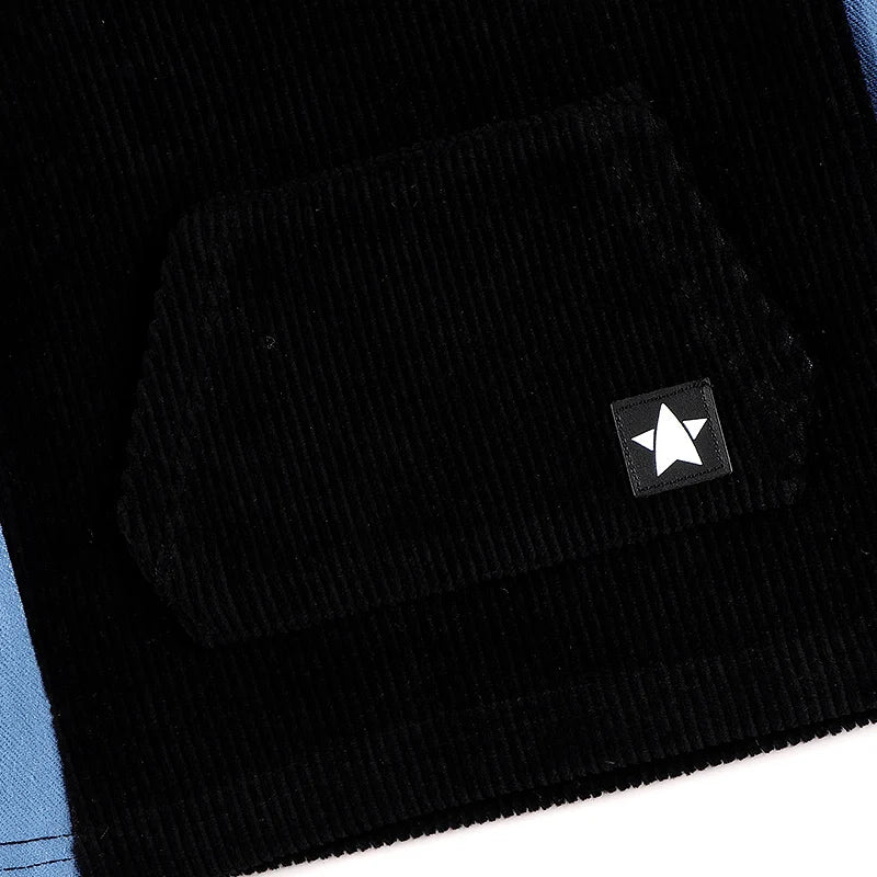 Close-up of kids black corduroy hoodie dress with denim side panel and kangaroo pocket showing fabric texture and star patch