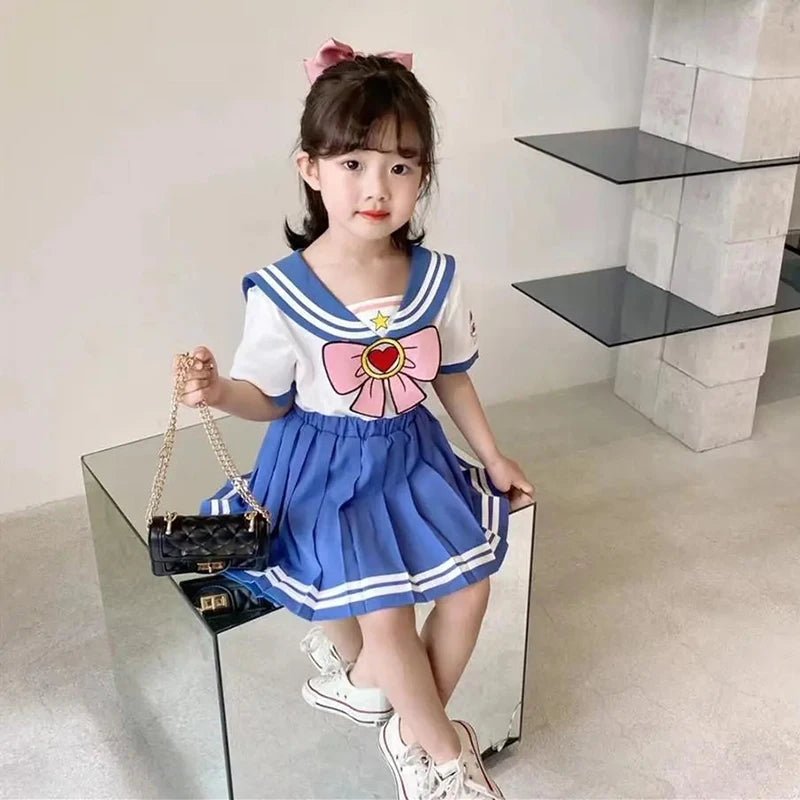 Kids Girls Cartoon Bow T-Shirt and Pleated Skirt Set Sailor Moon Cosplay Outfit worn by a young girl sitting with a black purse