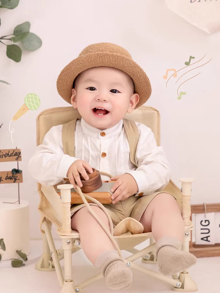 Adorable toddler boy wearing Boy Outfits Cotton Linen T-shirt and Shorts sitting on a beige chair with a hat