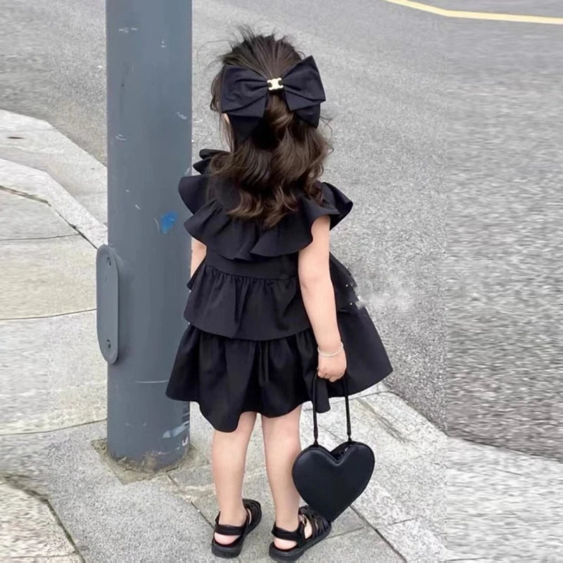 Girl wearing Korean Kids Summer Black Fly Sleeve Layered Dress Girls Fashion Outfit Clothes with black sandals and heart-shaped bag