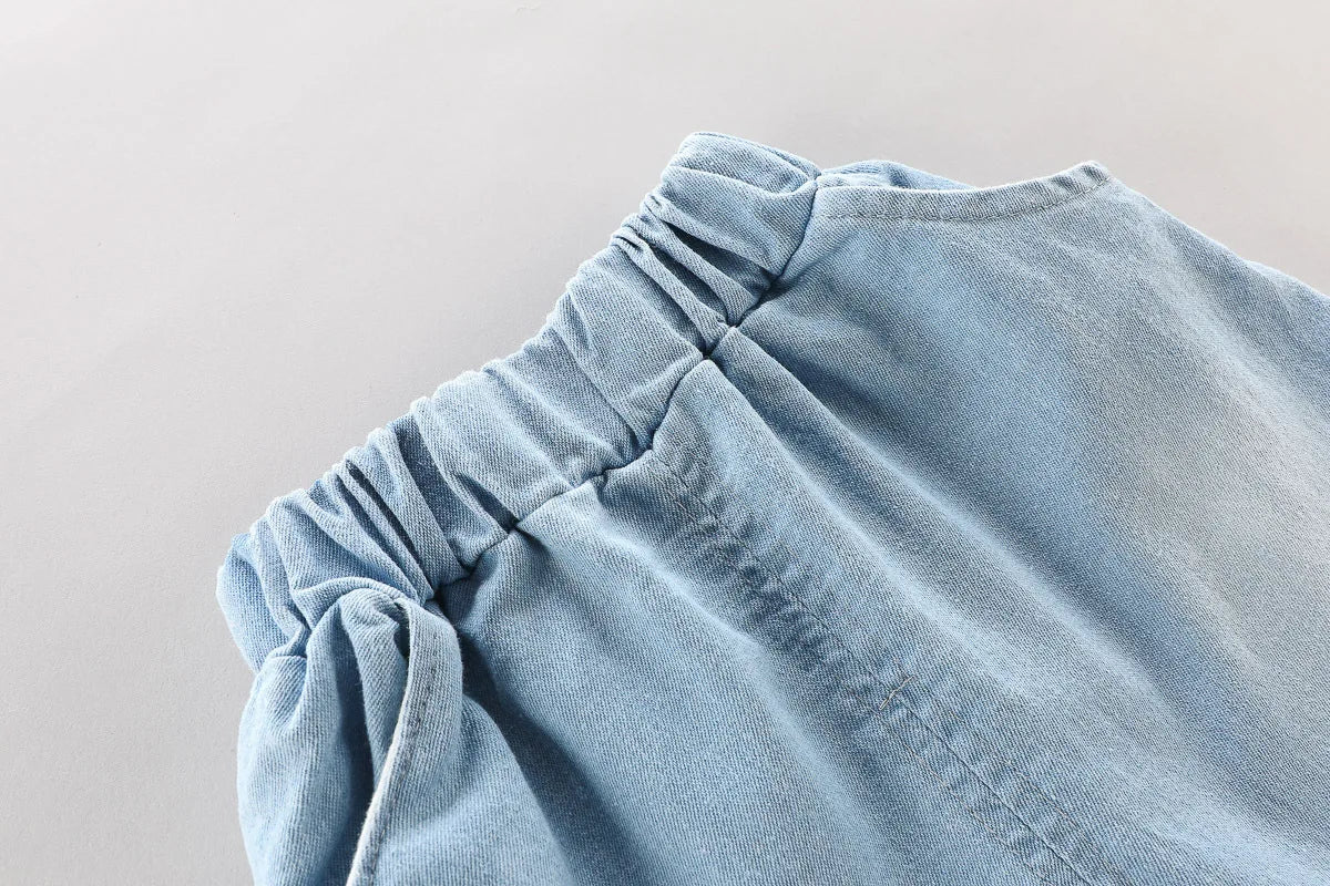 Close-up of light blue denim shorts with elastic waistband in toddler boys fashion outfit set printed t-shirt and cartoon bag