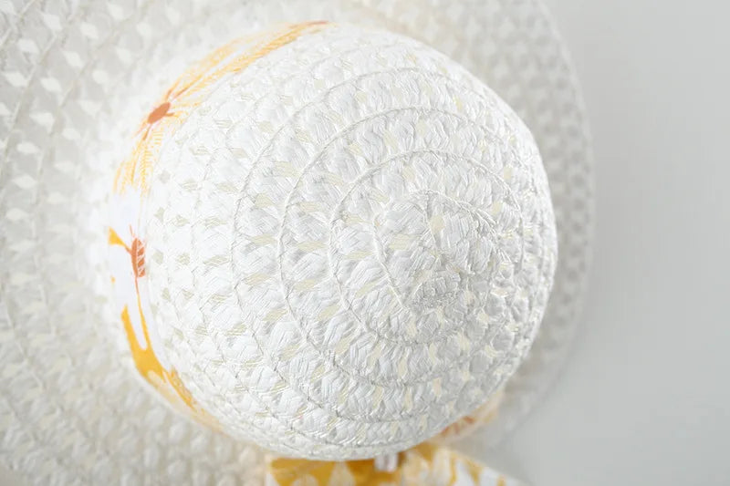 Close-up of a white woven sun hat with a yellow giraffe patterned ribbon for toddler girl clothes cotton beach